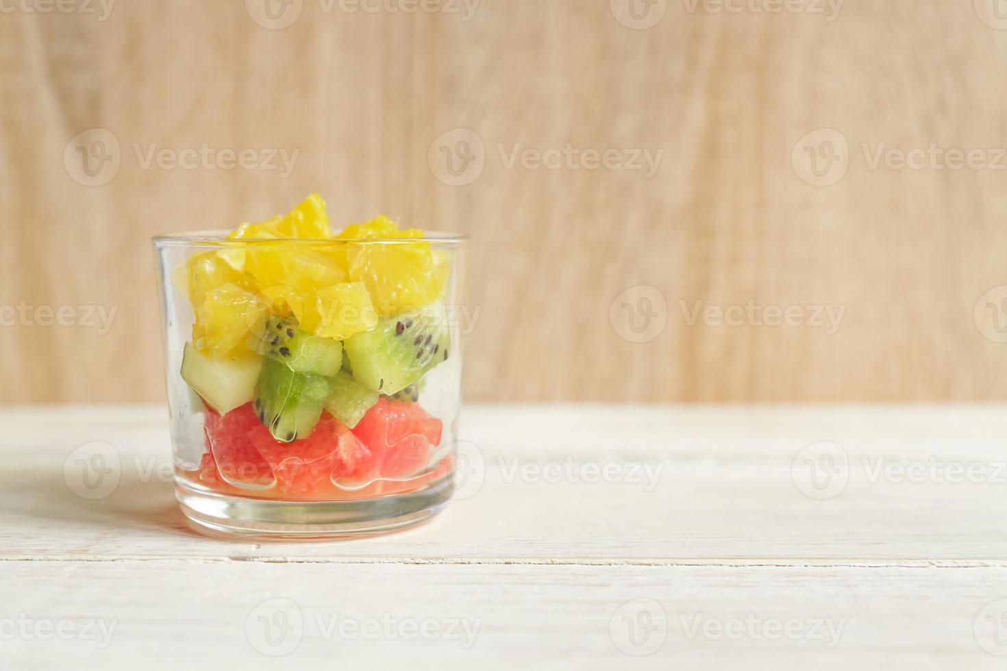 dieta ensalada de frutas mezcla fresca y sabrosa en un frasco de vidrio sobre una mesa de madera. naranjas jugosas picadas, kiwi y pomelos. foto