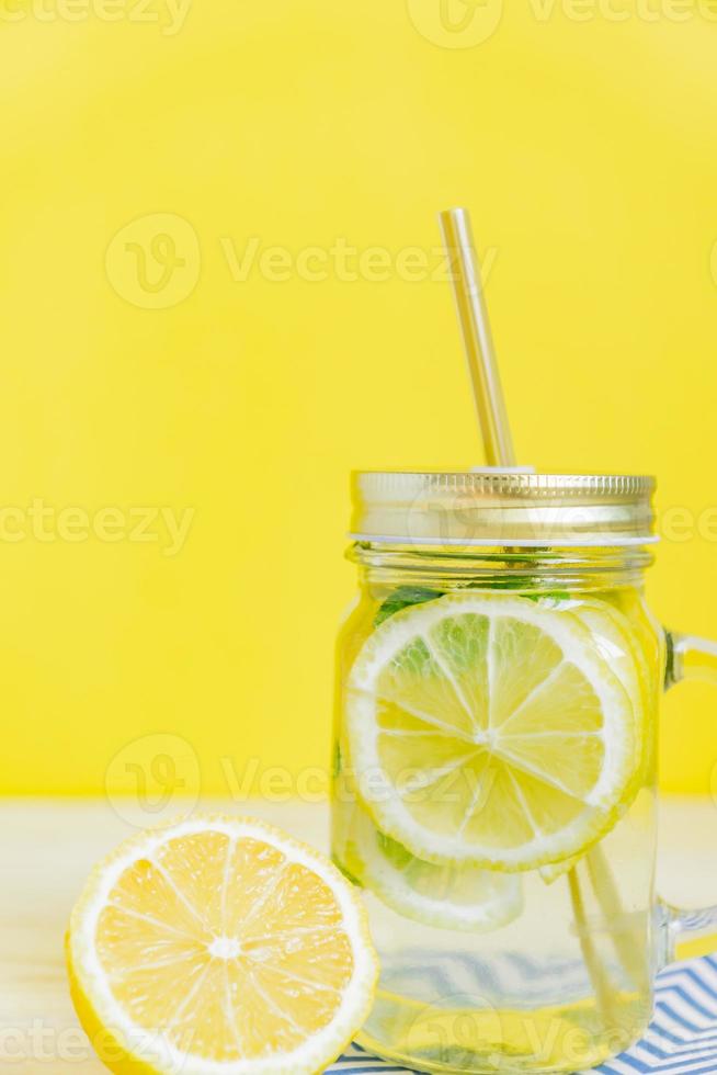 Citrus lemonade water with sliced lemon and mint, healthy and detox water drink in summer on yellow background. Summer bright backdrop with copy space photo