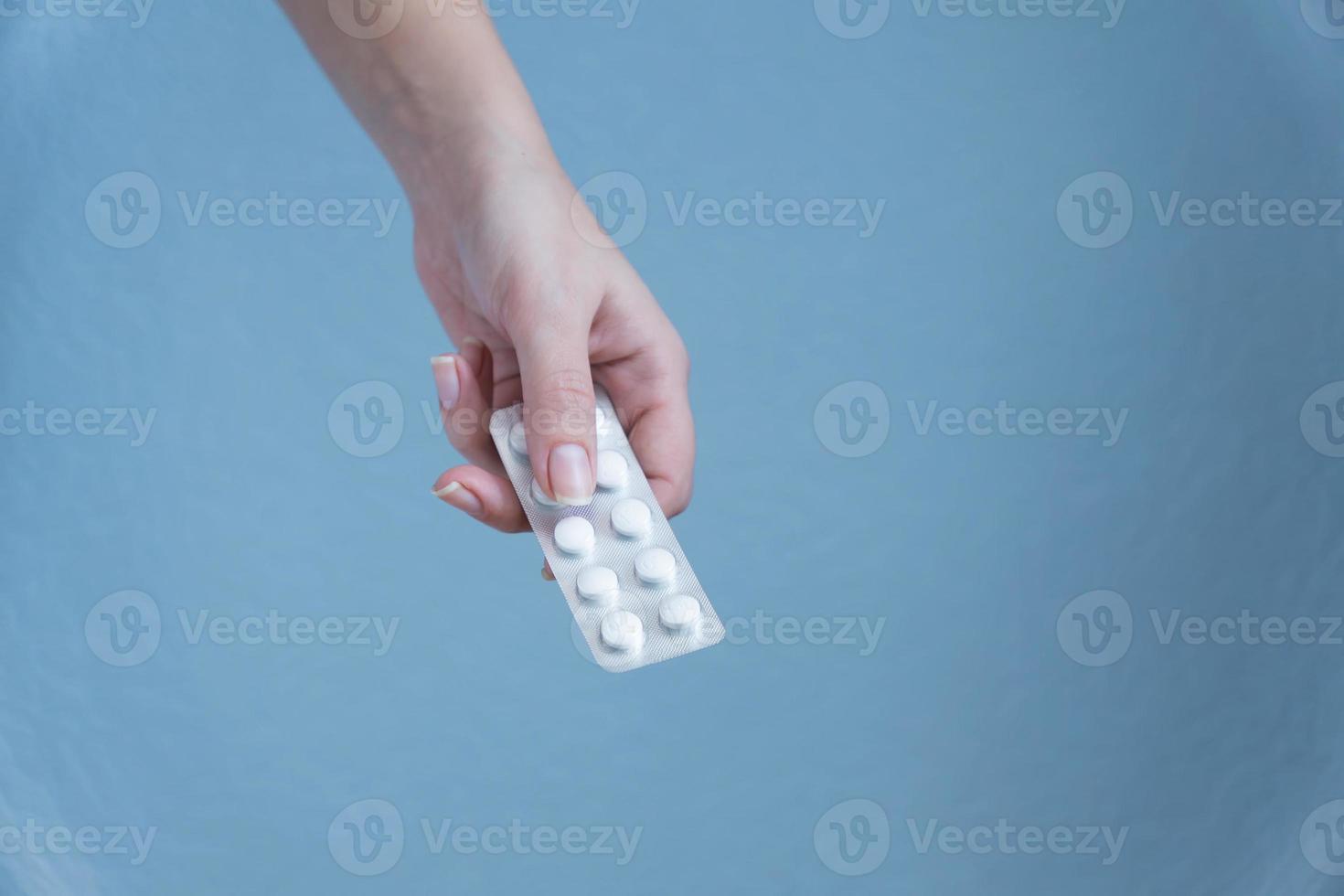 mano de mujer sosteniendo blister de pastillas sobre fondo azul. foto