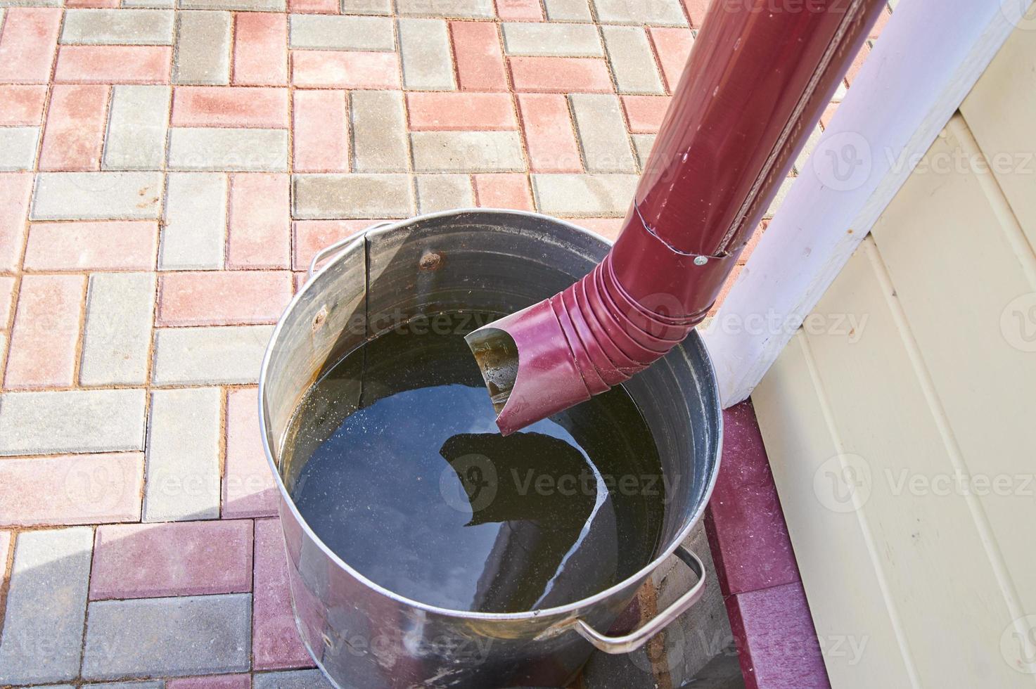 close up of gutter pipe and metal barrel full of water after the rain