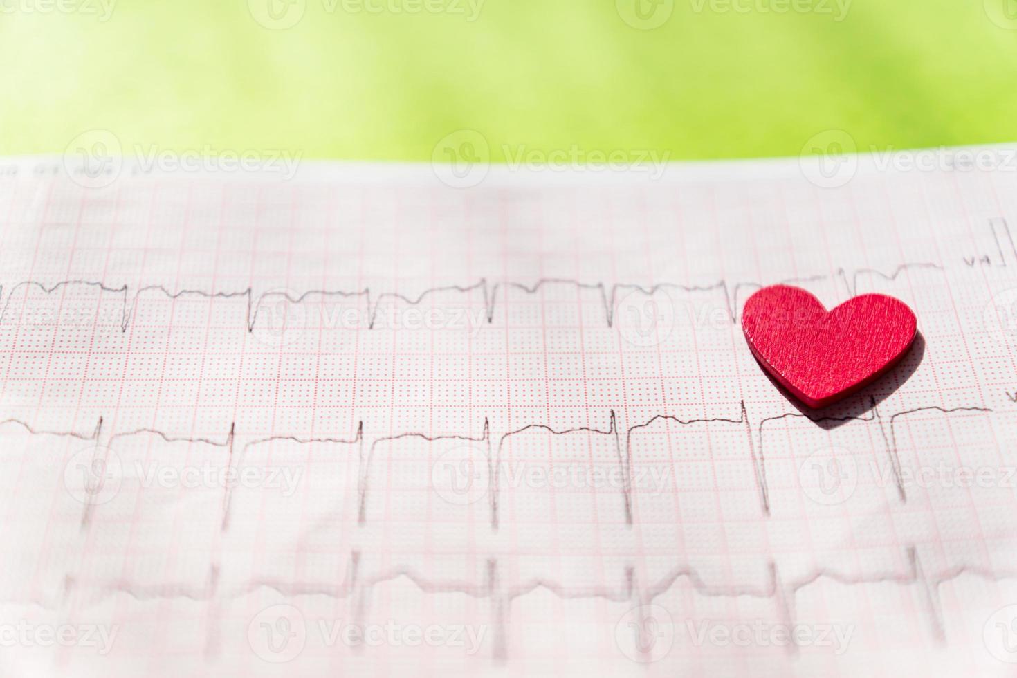 primer plano de un electrocardiograma en papel con corazón de madera roja. textura de fondo de papel ecg o ekg. concepto médico y sanitario. foto