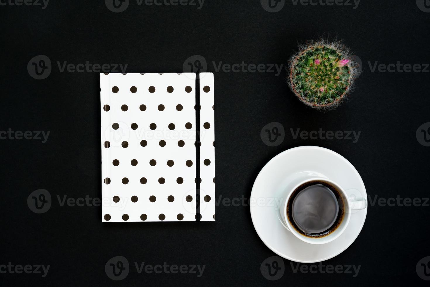 Cup of black coffee, notebook and blooming cactus on black background, Top view, copy space. photo