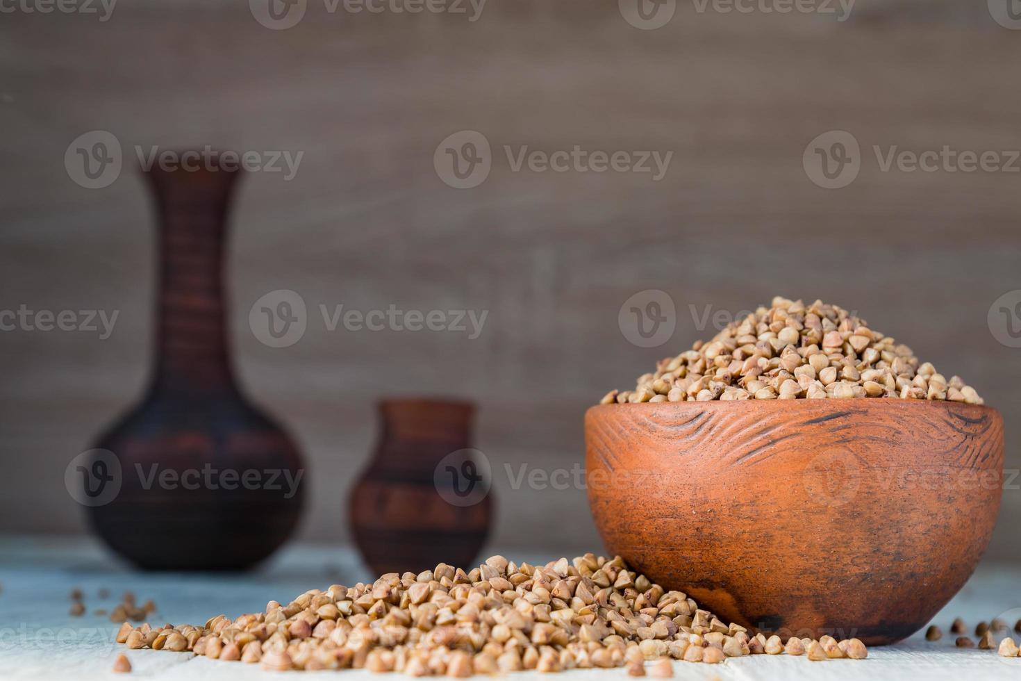 Dry buckwheat in brown clay bowl on wooden table. gluten free grain for healthy diet photo