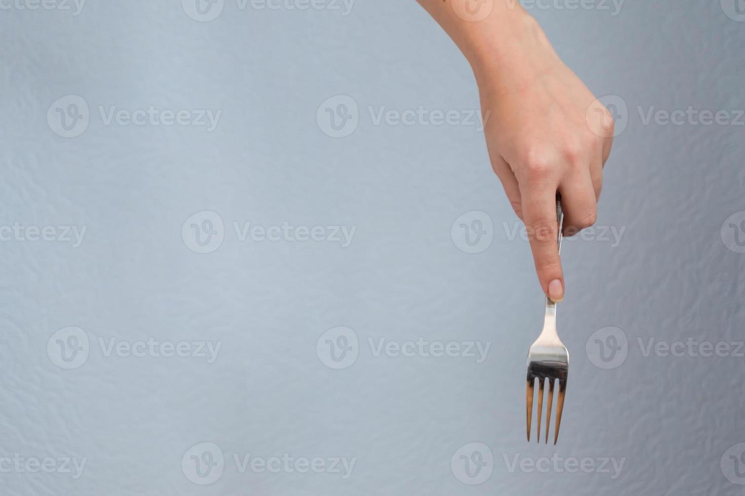 woman hand holding fork on gray background. Eating gesture. photo