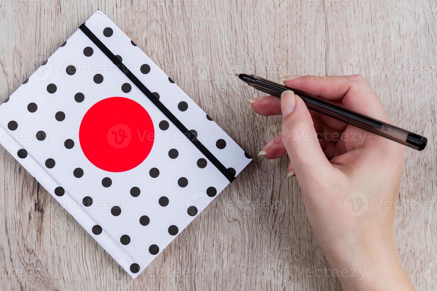 young woman hand hold black pen and polka dot cover notebook on  wooden table photo