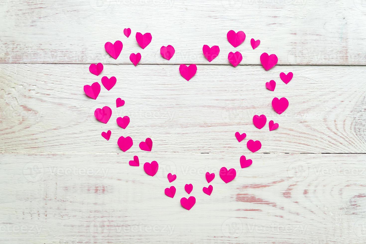 gran corazón rosa hecho de papel recortado pequeños corazones sobre fondo de madera. decoración hecha a mano para el día de san valentín. foto
