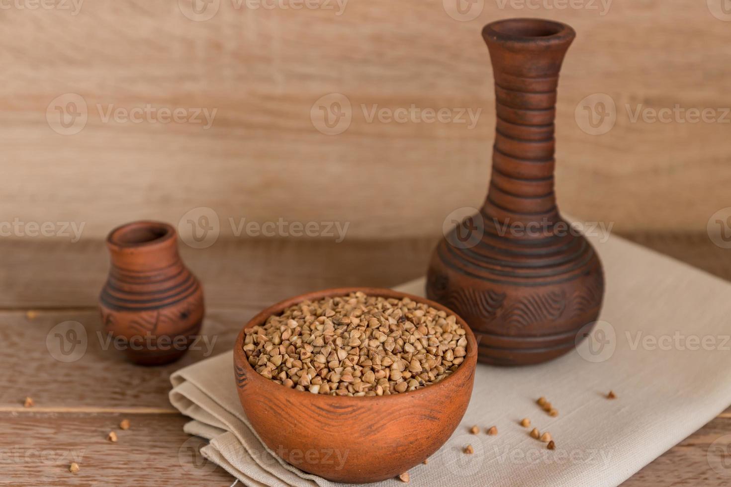 Dry buckwheat in brown clay bowl on wooden table. gluten free grain for healthy diet photo