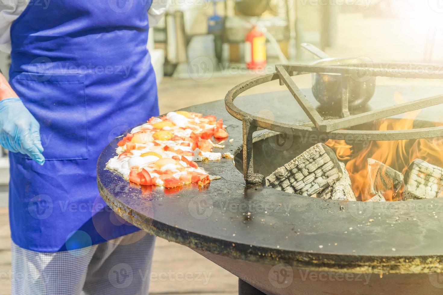 chef cocina huevos fritos con tomates en el festival. comida callejera preparada a la parrilla foto