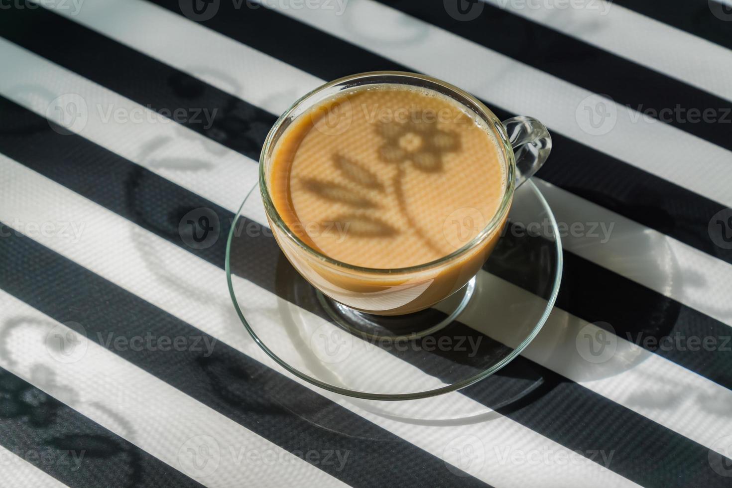 transparent cup of creamy coffe on dark background. Sunlight and hard shadows. Toned image with copy space photo