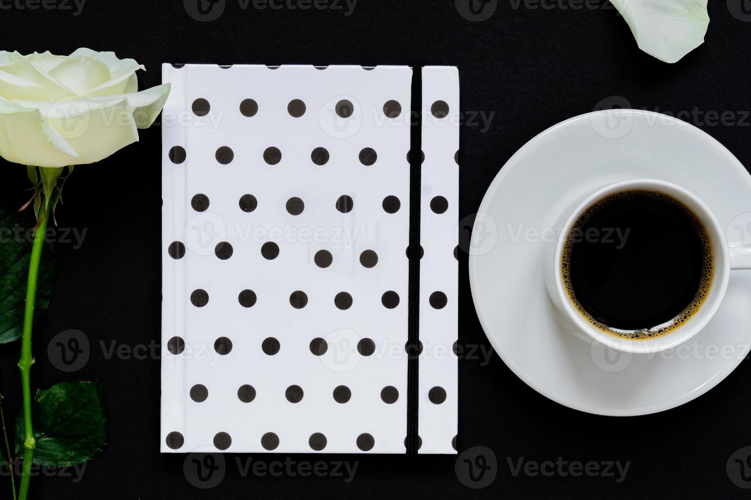 Cup of black coffee, notebook and white rose on black background, Top view, copy space. photo