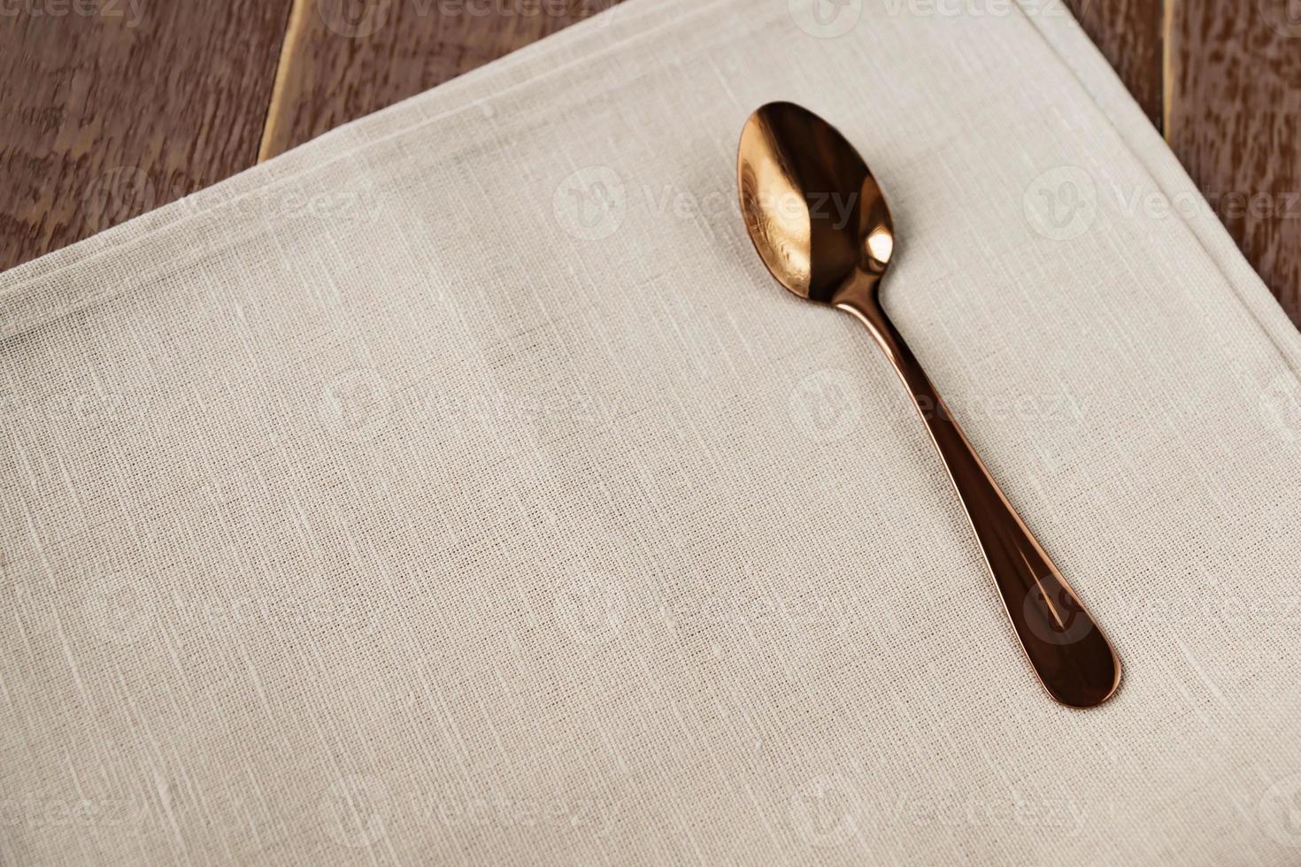 Top view of cloth napkin of beige color and served tea spoon on wooden table. photo