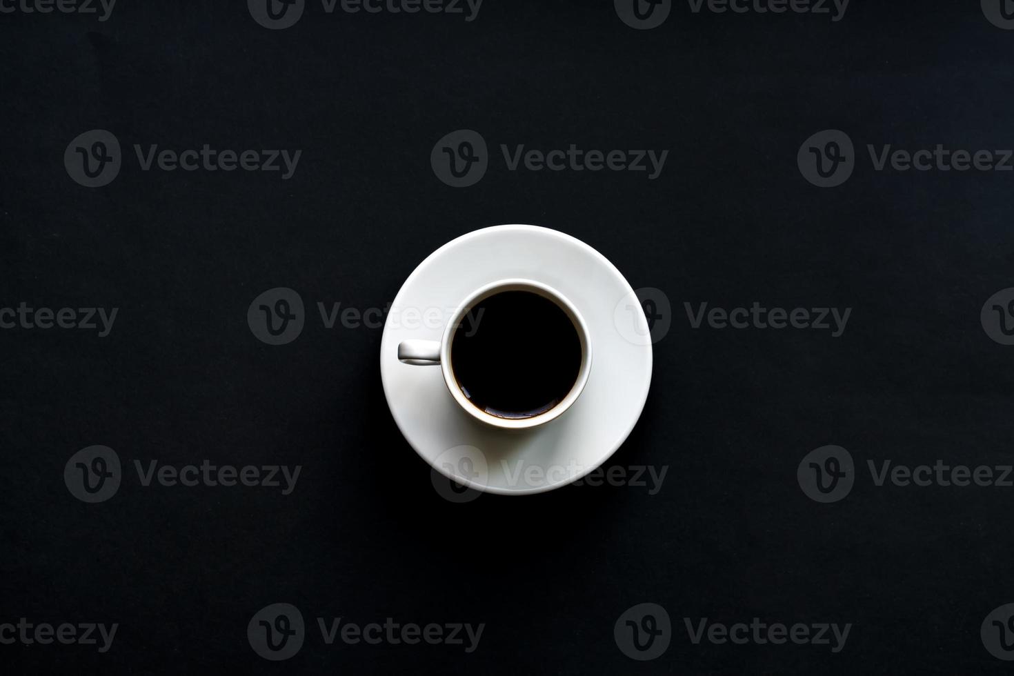 top view of white cup of coffee on black background. Minimal flat lay. photo