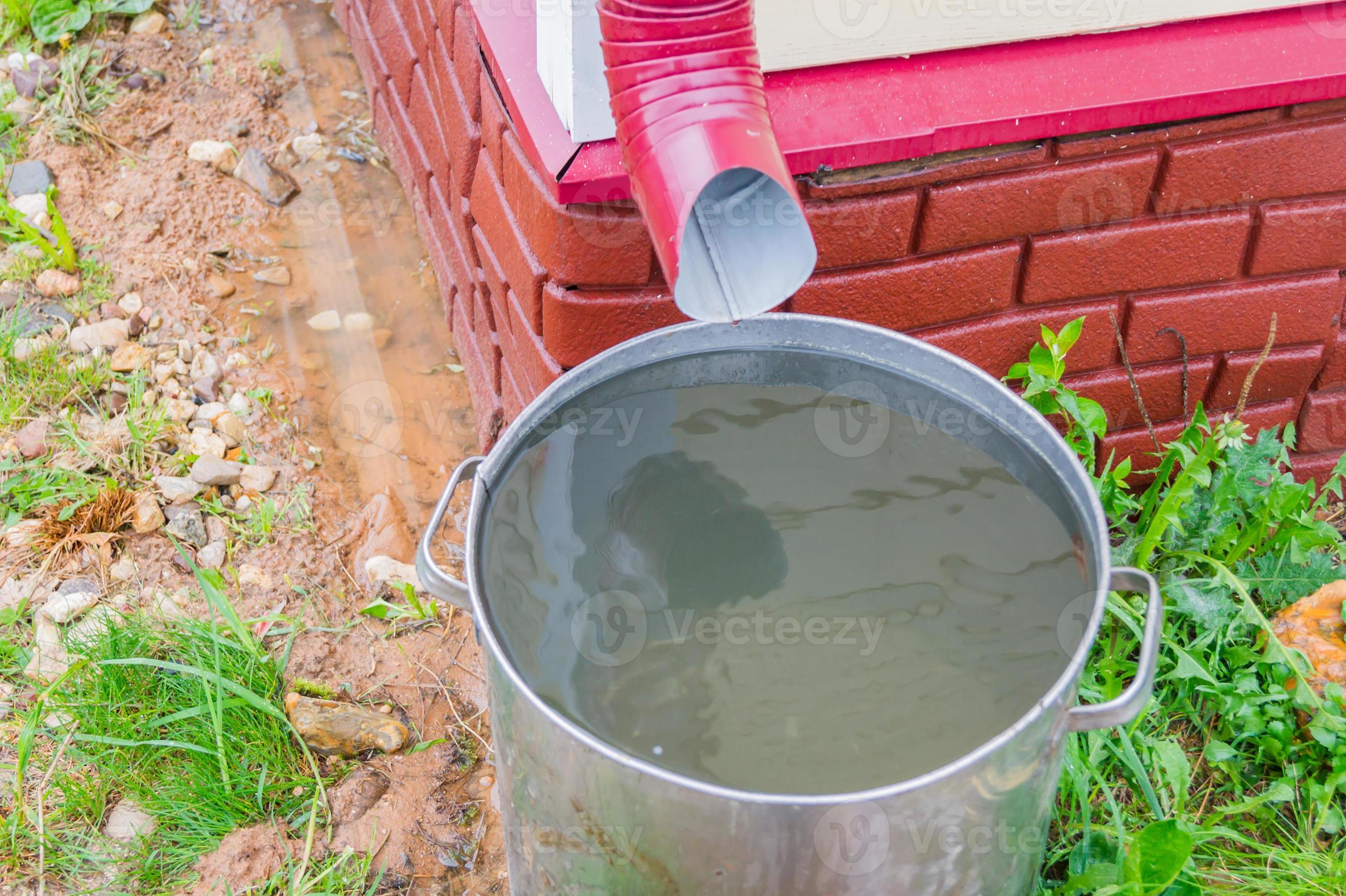 close up of gutter pipe and metal barrel full of water after the rain