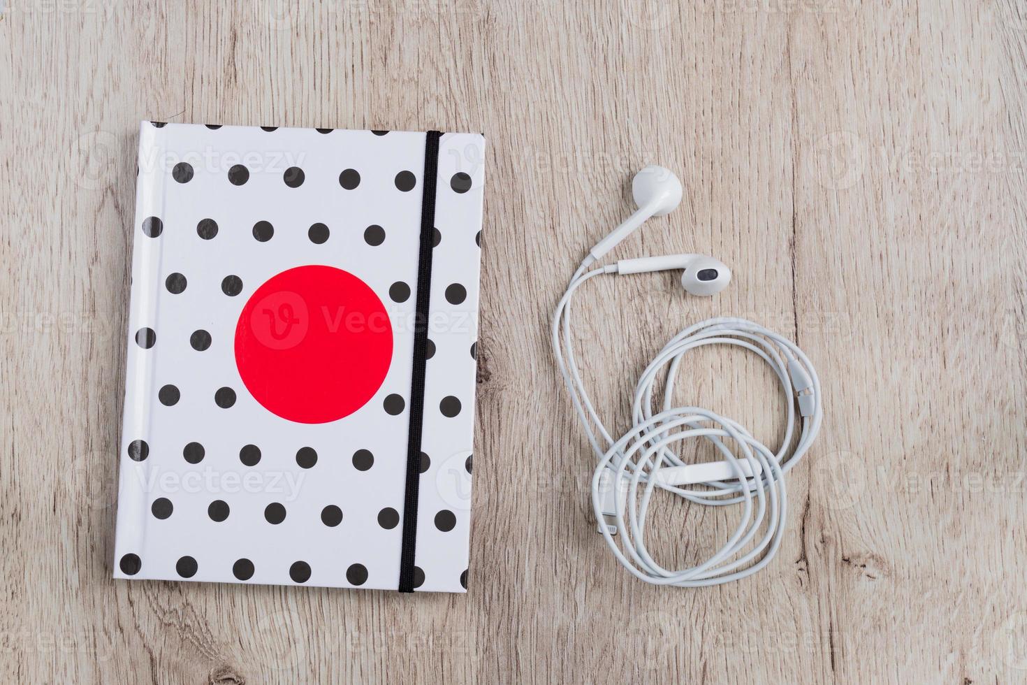 Top view of hotebook with polka dot cover and white headphones on wooden table. Minimal flat lay. photo