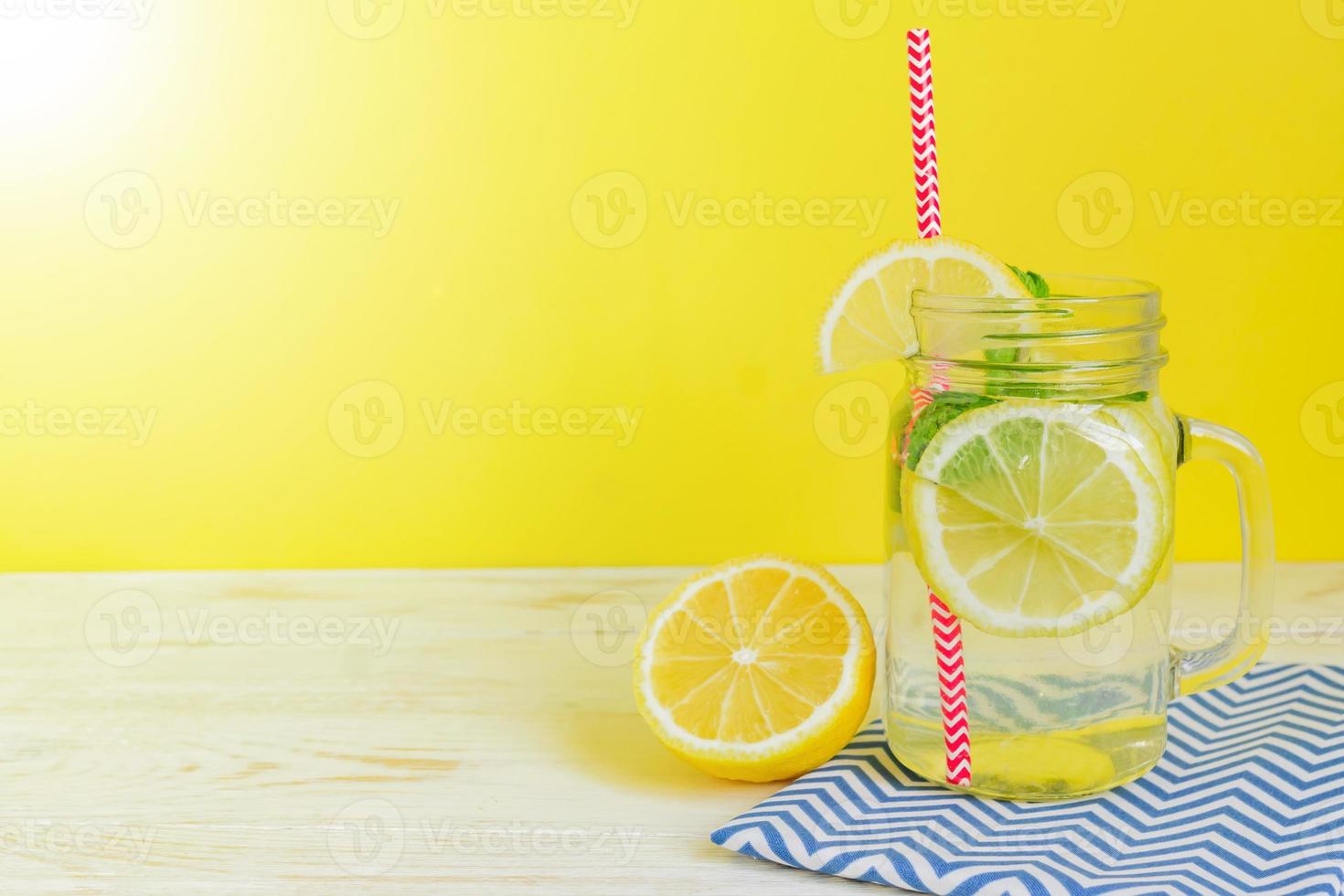 Citrus lemonade water with sliced lemon and mint leaves, healthy and detox water drink in summer on wooden table with bright yellow  background photo