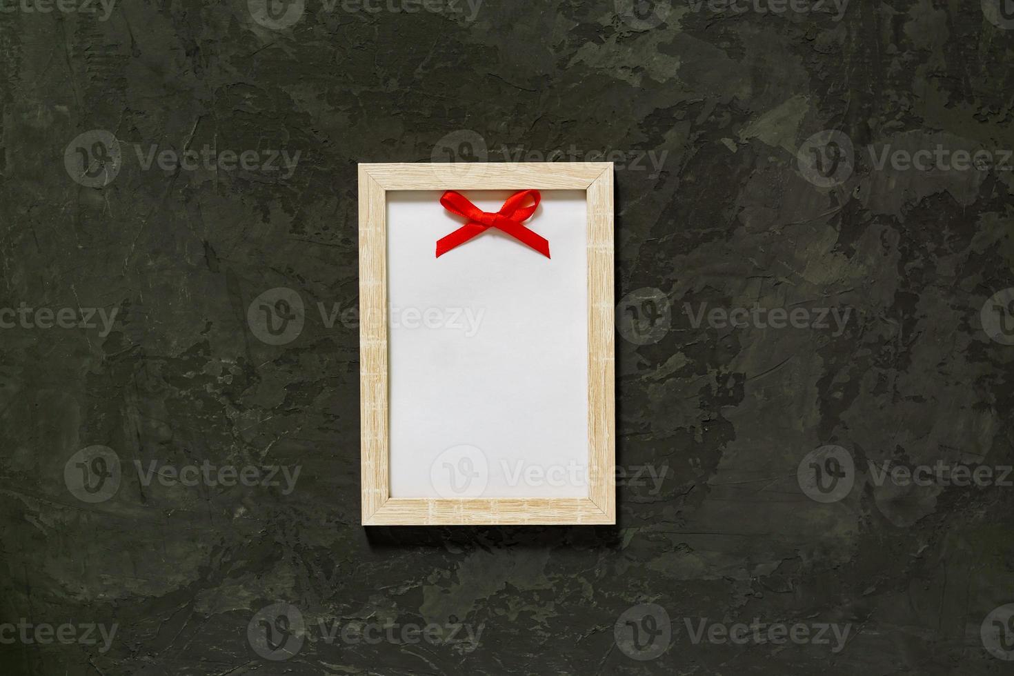 Wooden photo frame with red satin bow on black background. Mockup.