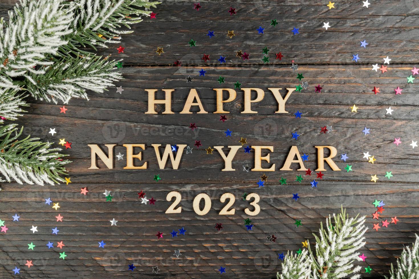 New Year's concept. Heppy new year 2023 wooden text on a wooden background, fur-tree branch on the edge of the frame photo