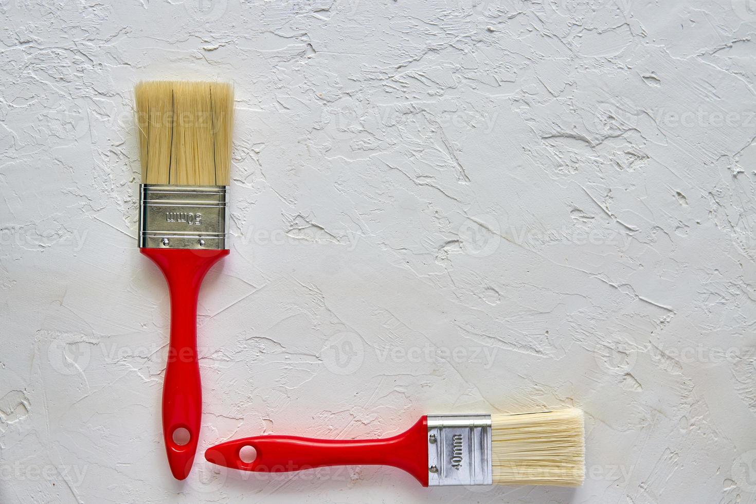 two paintbrushes with red handles on freshly made concrete background. Repairing concept. Top view with copy space photo