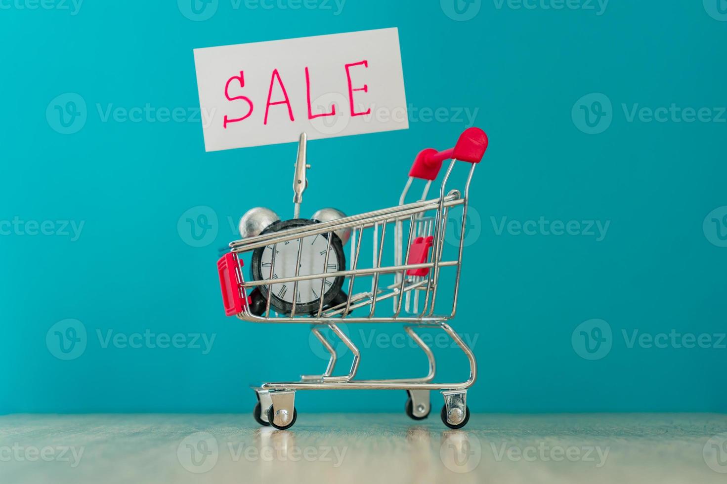 Alarm clock and banner with handwritten world SALE on wooden table. Shopping concept. photo