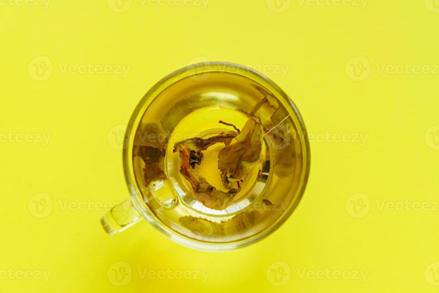 top view of transparent cup with green tea on yellow background. photo