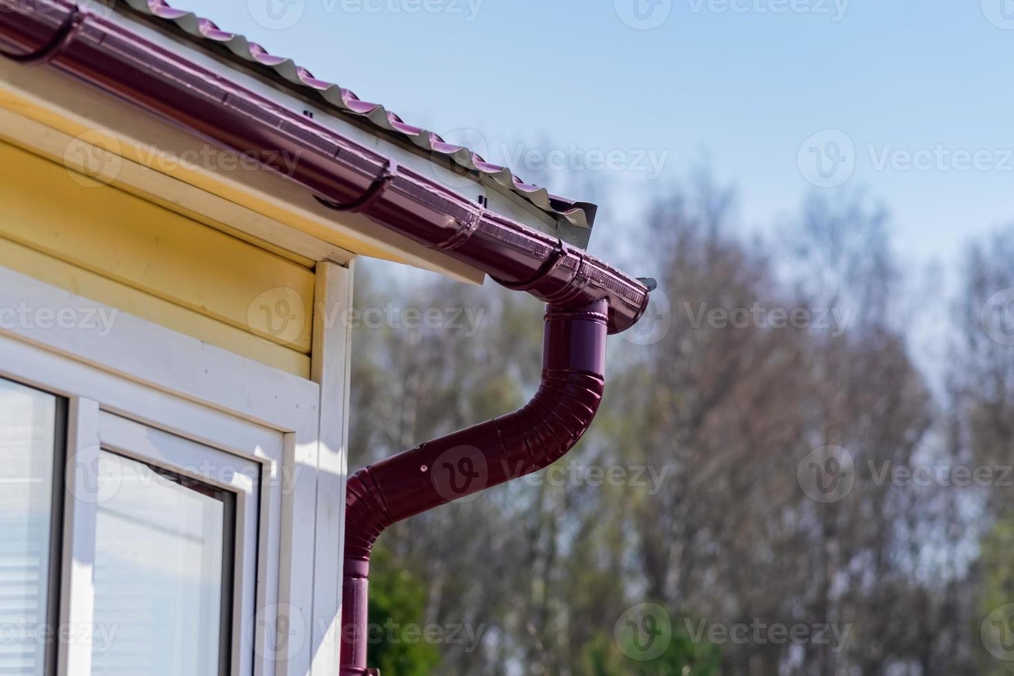 Corner of the house with gutter on a background of blue sky and spring forest photo