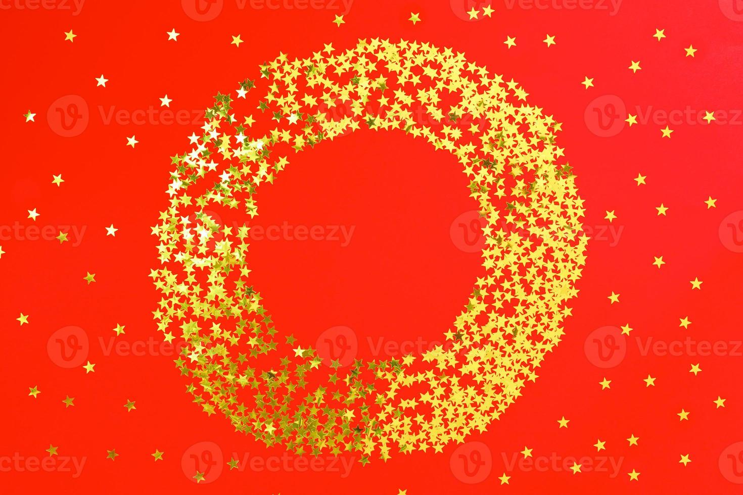 Red backdrop with glitter and golden stars confetti in circle. Festive holiday bright background photo