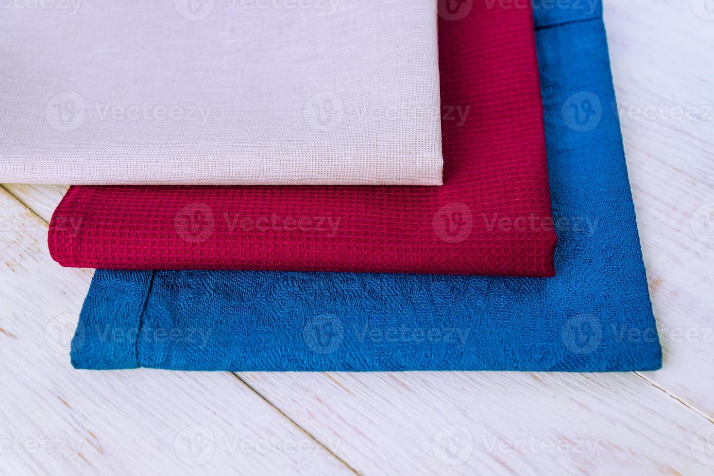 close up of cloth napkins of beige, blue and burgundy colors on rustic white wooden table. Shallow depth of field. photo