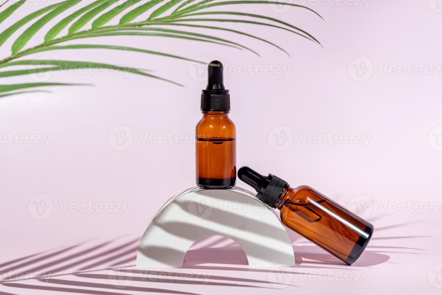 Amber dropper bottlesa on light pink background. Care about face, hands and body skin. Women beauty product. Empty place for logo on bottle. Hard light and palm leaf. photo