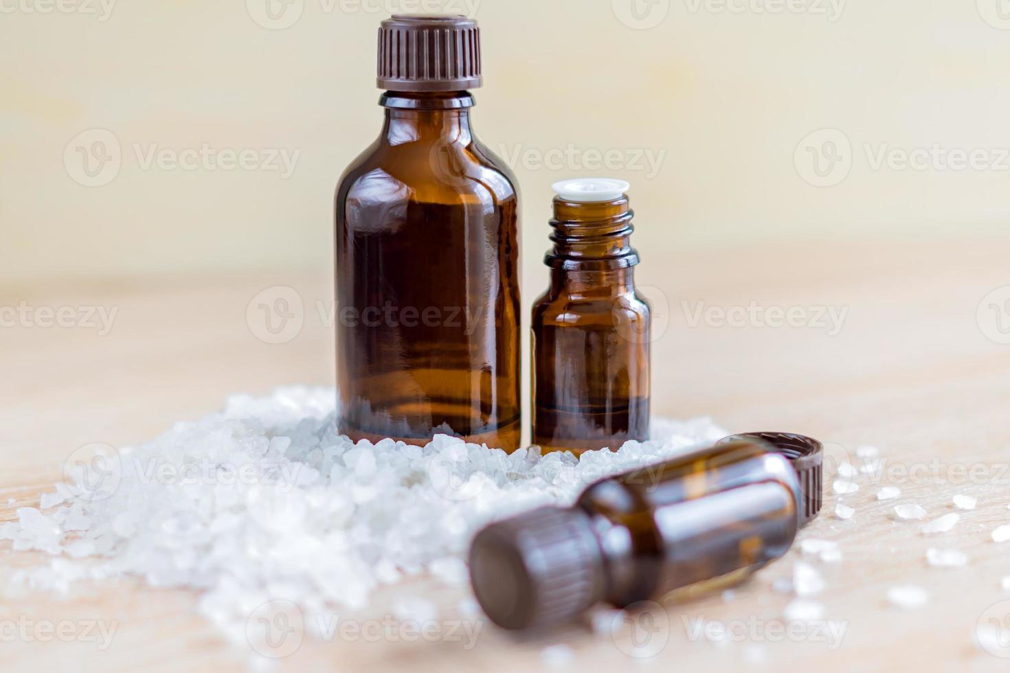 Pile of sea salt and bottles with aromatic essential oil on wooden table. Natural ingredients for spa and exfoliation. photo
