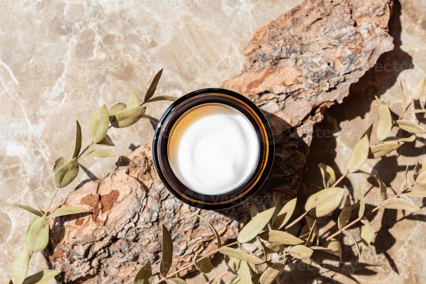 dark glass jar with cream with peptides, branch of dried eugalyptus on marble table. Herbal aromatherapy and skincare photo