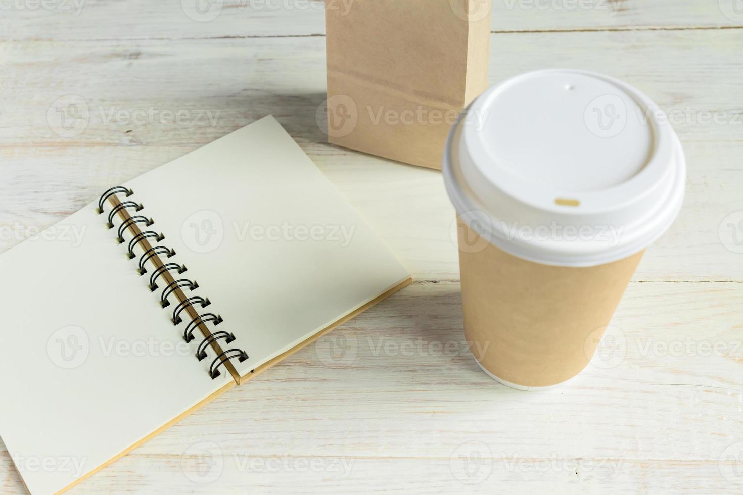 Open Notebook and brown paper craft cup of coffee to go on white wooden table with copy space. Eco and recycling concept photo