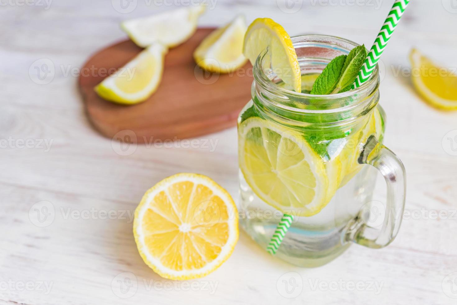 Mason jar glass of homemade lemonade with lemons, mint and green paper straw on wooden rustic background. Summer refreshing beverage. photo