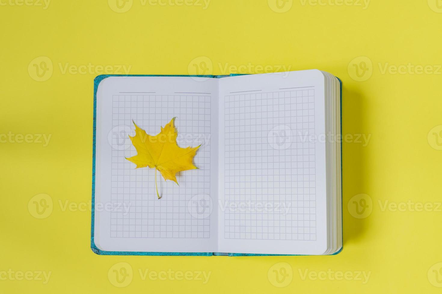 Blank open notebook with maple leaf  on yellow background. Empty diary and autumn concept photo