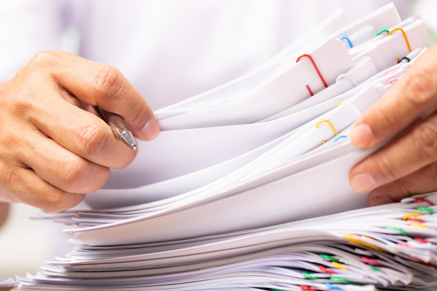 Close-up hands of a man in a white shirt searching for contract agreement documents in Stack of Group report papers clipped in color clips photo