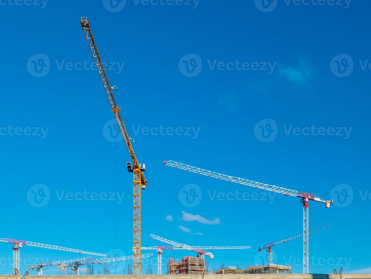 Construction cranes work on creation site against blue sky background. Bottom view of industrial crane. Concept of construction of apartment buildings and renovation of housing. Copy space photo