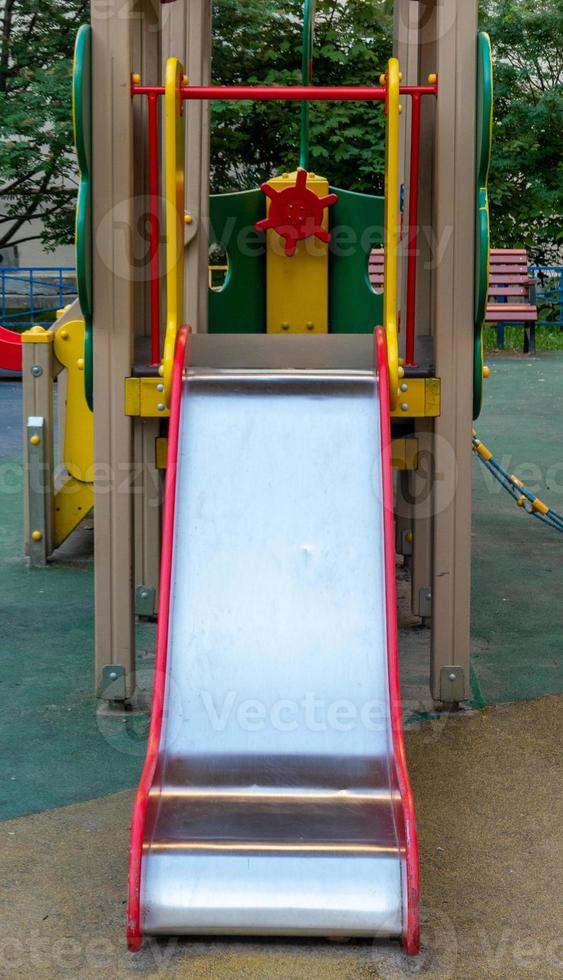 un elemento de un columpio para niños. deslizar. un colorido parque infantil al aire libre junto a la casa. un dia de verano parque infantil con suelo de goma. foto