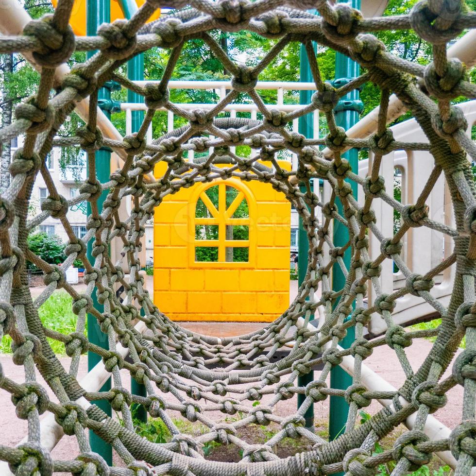 Inside view of a long rope mesh pipe, at the end of the tunnel yellow playground blurred background photo