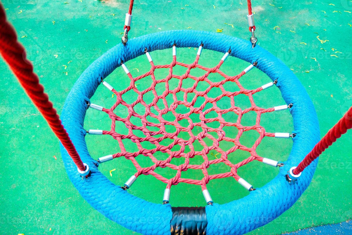 Round swing seat made of mesh in playground. Empty blue rope web nest for swinging closeup. photo