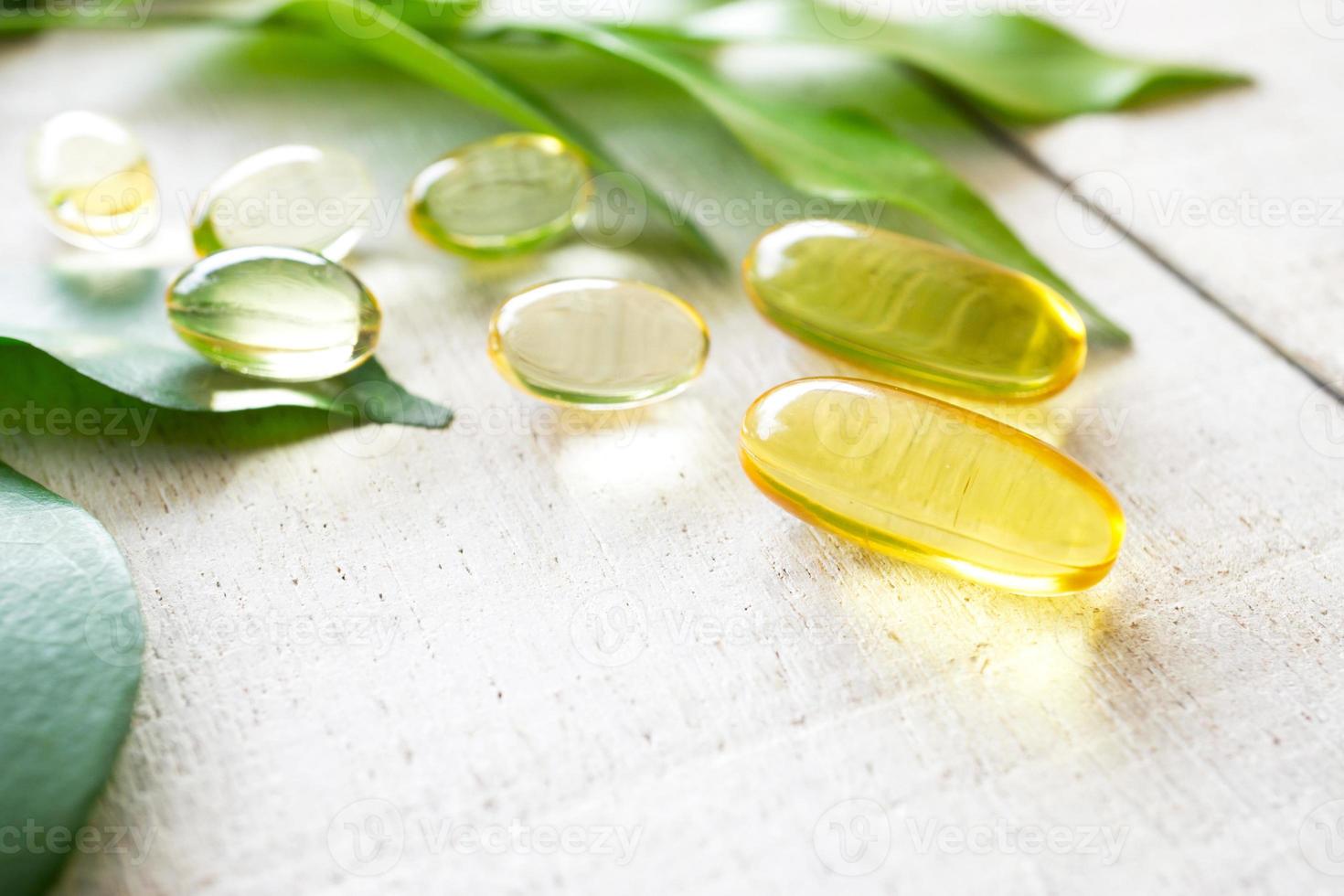 Natural vitamins supplement on white wood background with green leaves. photo