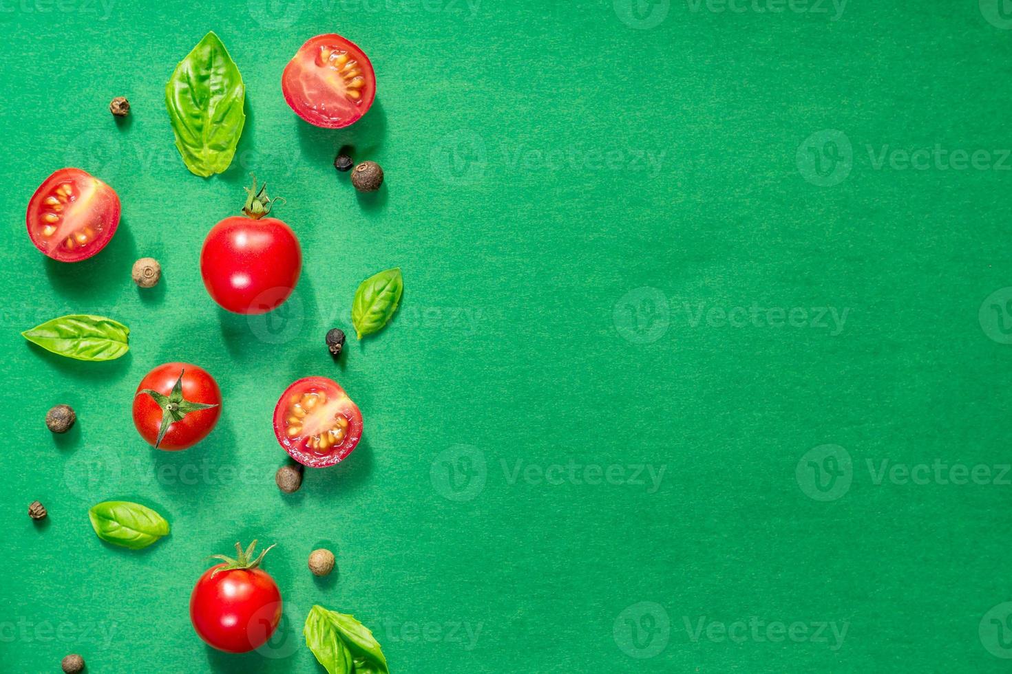 Halved Juicy Cherry Tomatoes and Basil Leaves on a green background. Concept for healthy nutrition. Top view. Copy space. photo