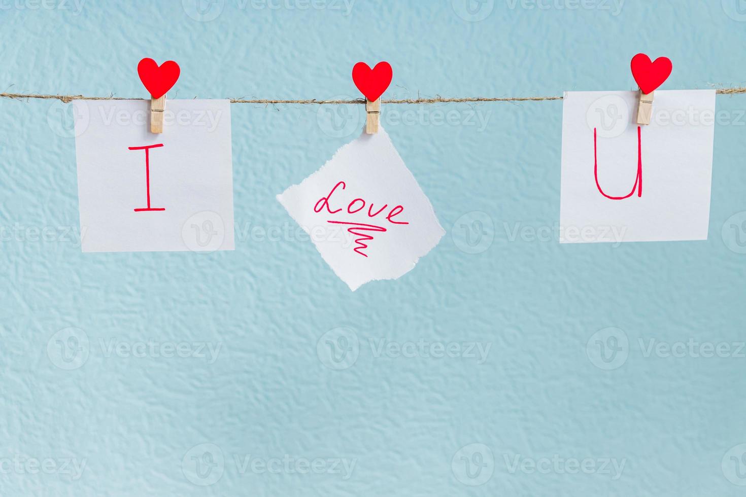 alfileres de corazones de amor de san valentín rojo colgando de un cordón natural sobre fondo azul. te amo inscripción en piezas de papel. foto