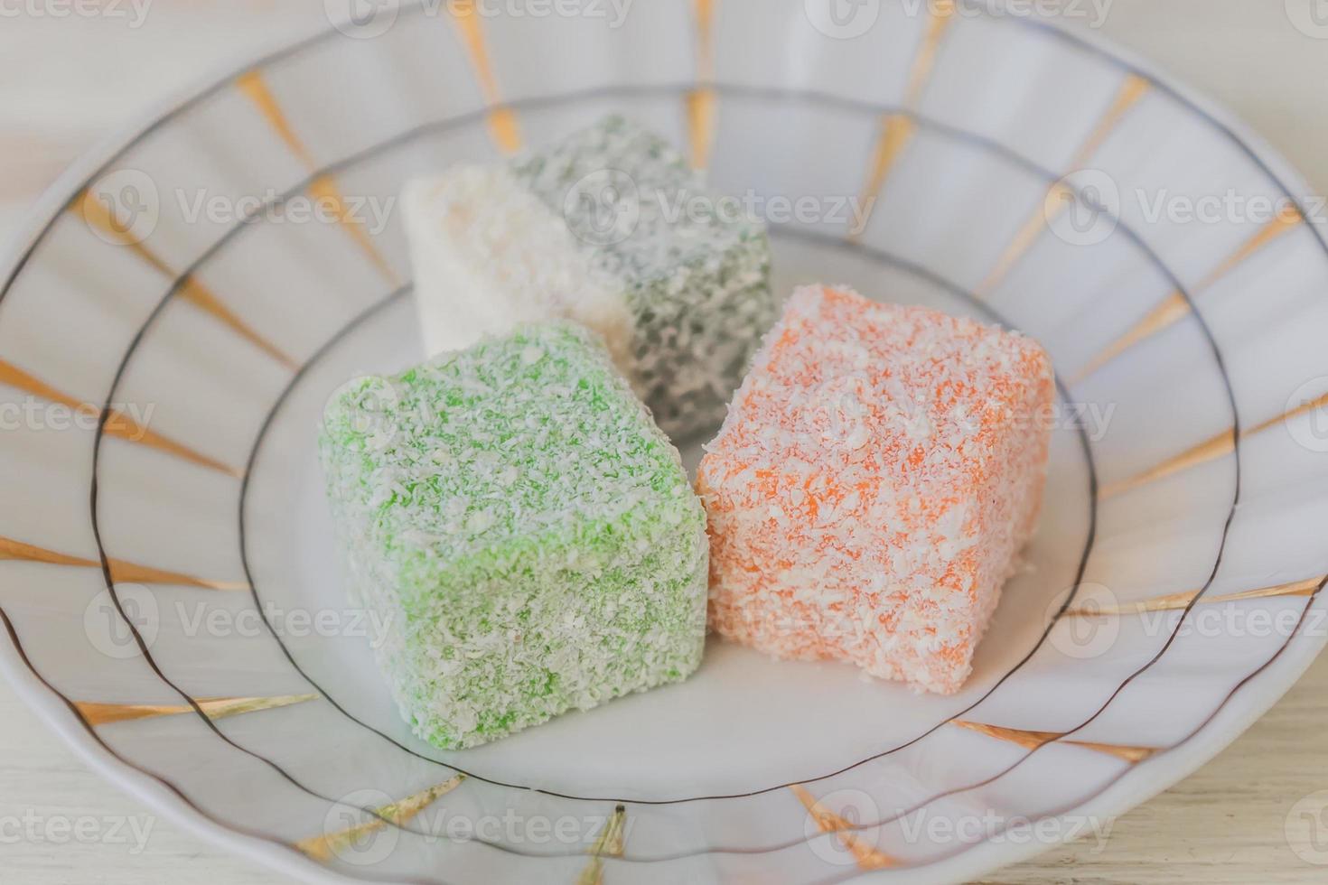 Traditional turkish delight on a plate on white wooden background. Assorted Oriental sweets. photo