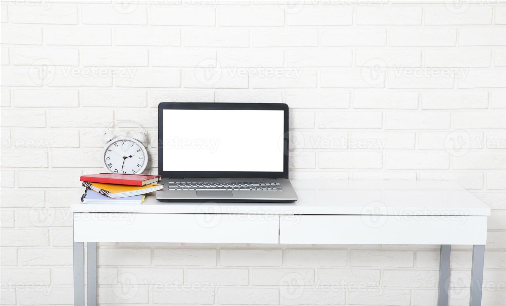 accesorios educativos en la mesa cerca de la pared de ladrillo. computadora vacía y pantalla móvil con lugar para texto. foto