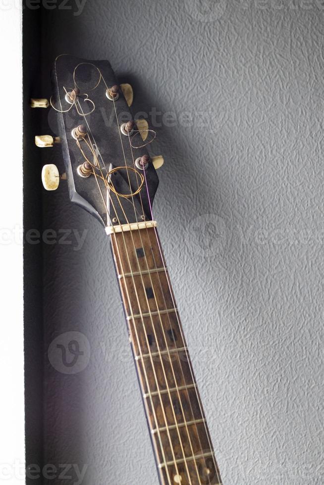 An acoustic old guitar in dust stands against a gray wall with copy space. Background for a screensaver with a musical instrument in the old style. Vertical photography. photo