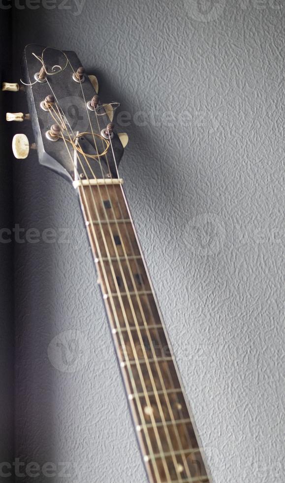 An acoustic old guitar in dust stands against a gray wall with copy space. Background for a screensaver with a musical instrument in the old style. Vertical photography. photo