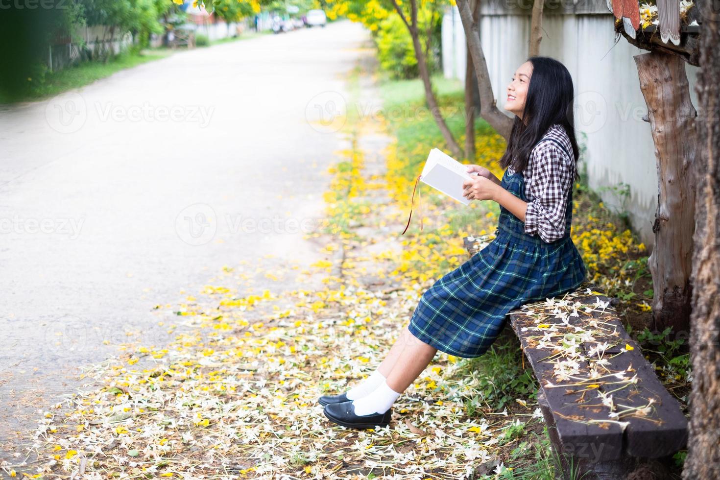 Young girl sitting on a bench reading a book under a beautiful tree. photo