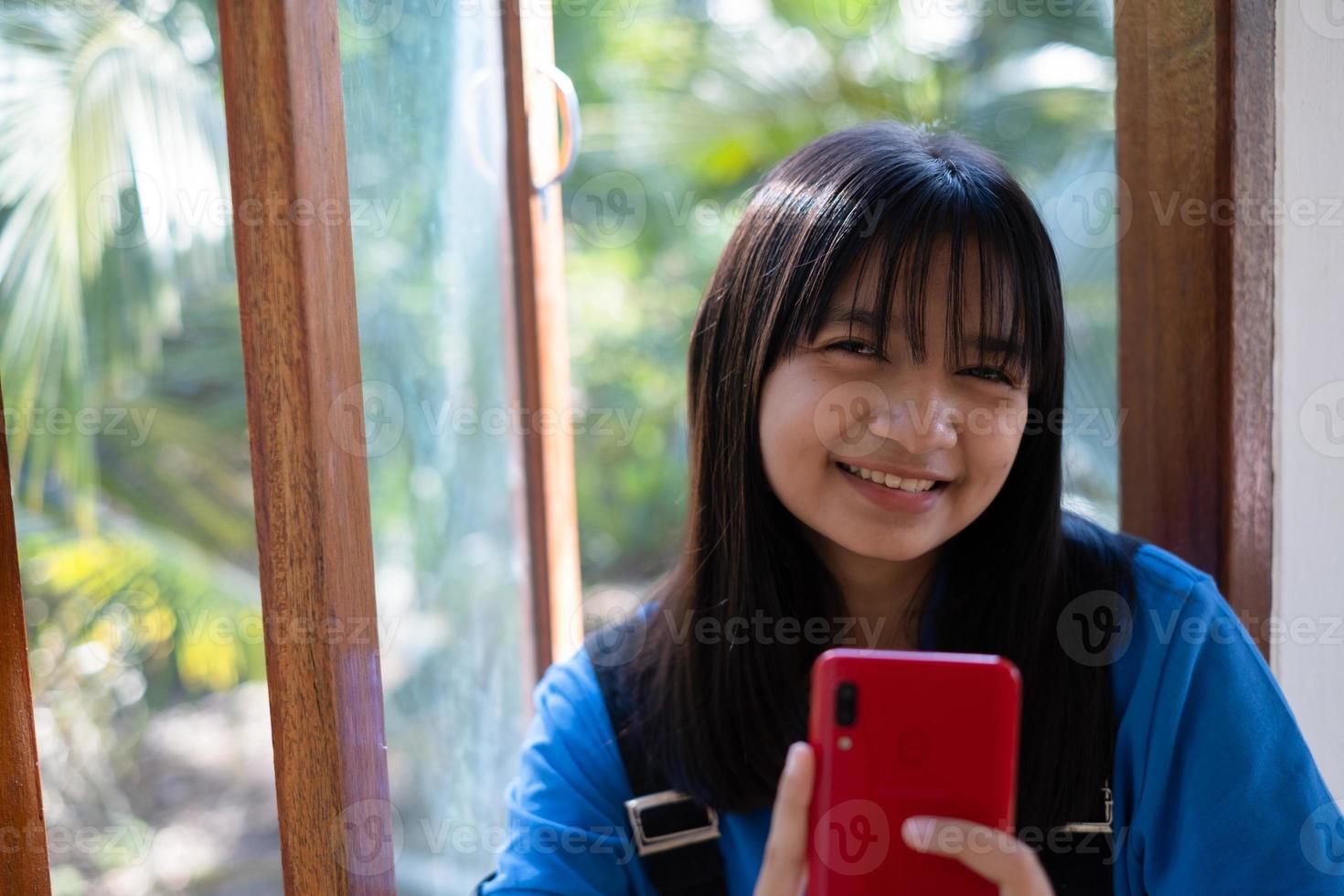 niña feliz usando teléfono móvil y sentada en las ventanas en casa. foto