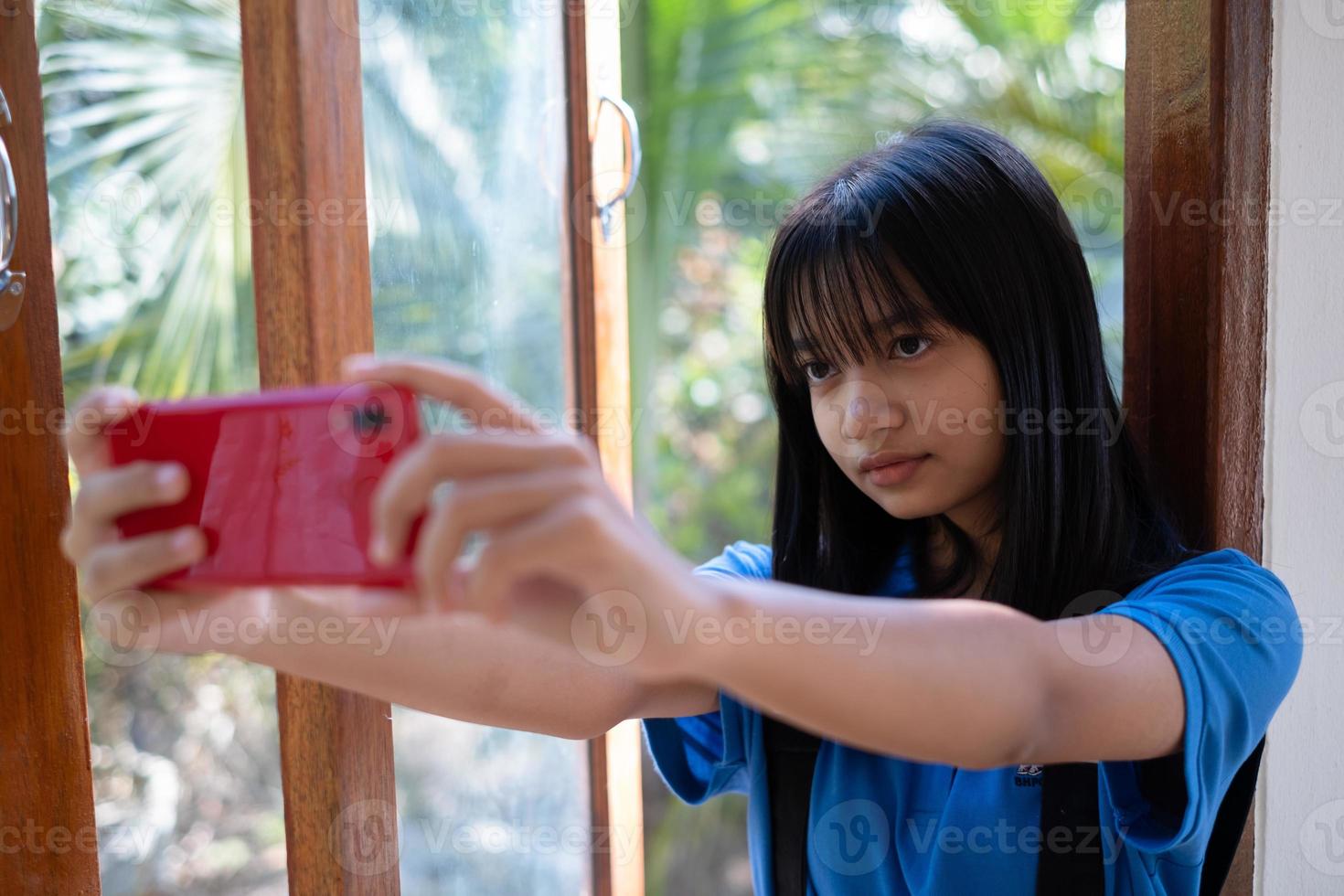 Happy young girl using mobile phone and sitting on the windows at home. photo