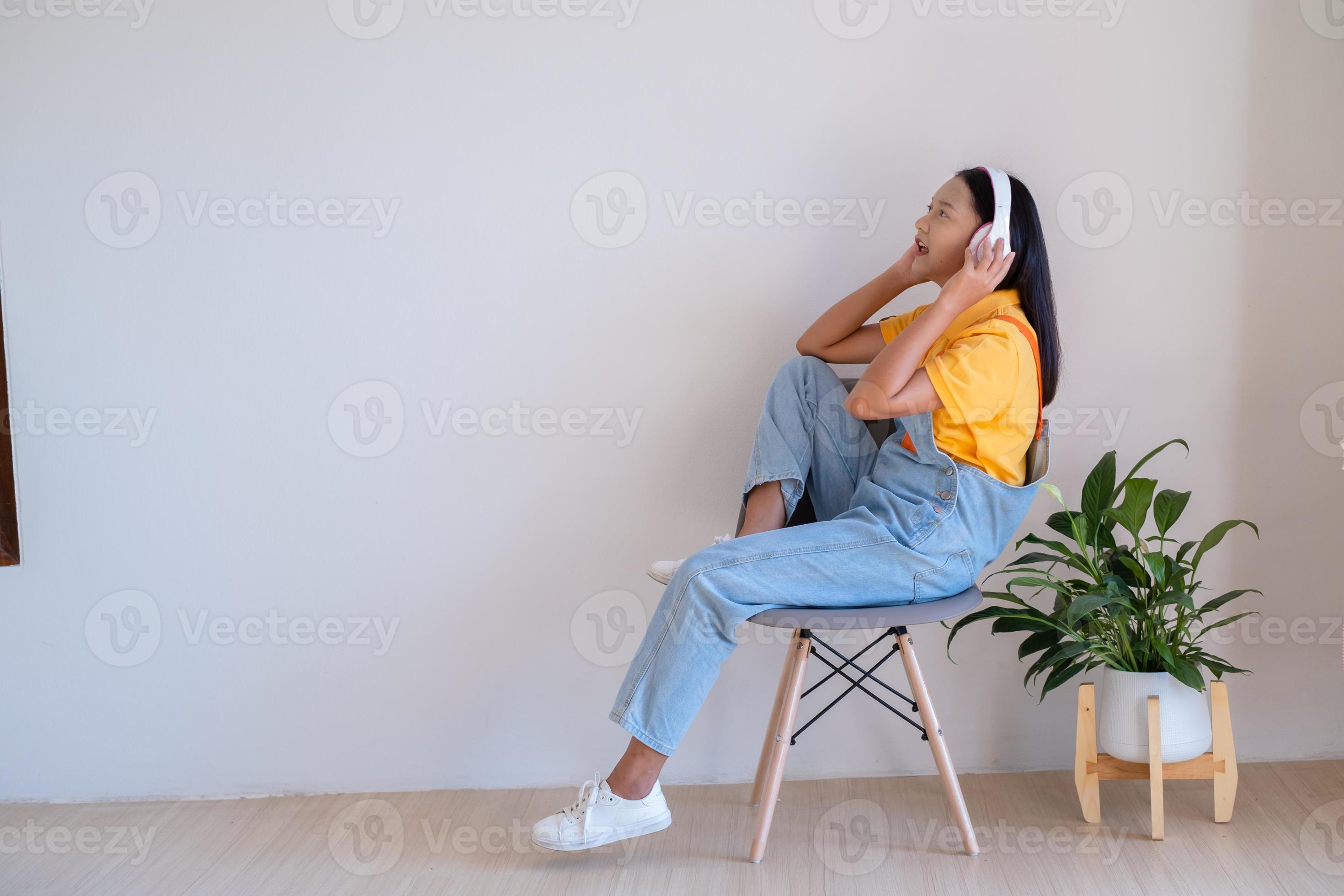 The happy girl sitting on a chair listening to music in minimal room at