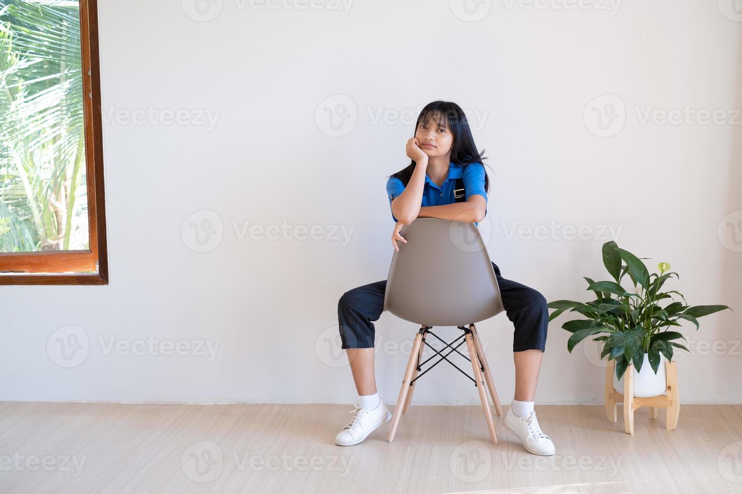 la chica sentada en la silla gris con planta verde en una habitación mínima. foto